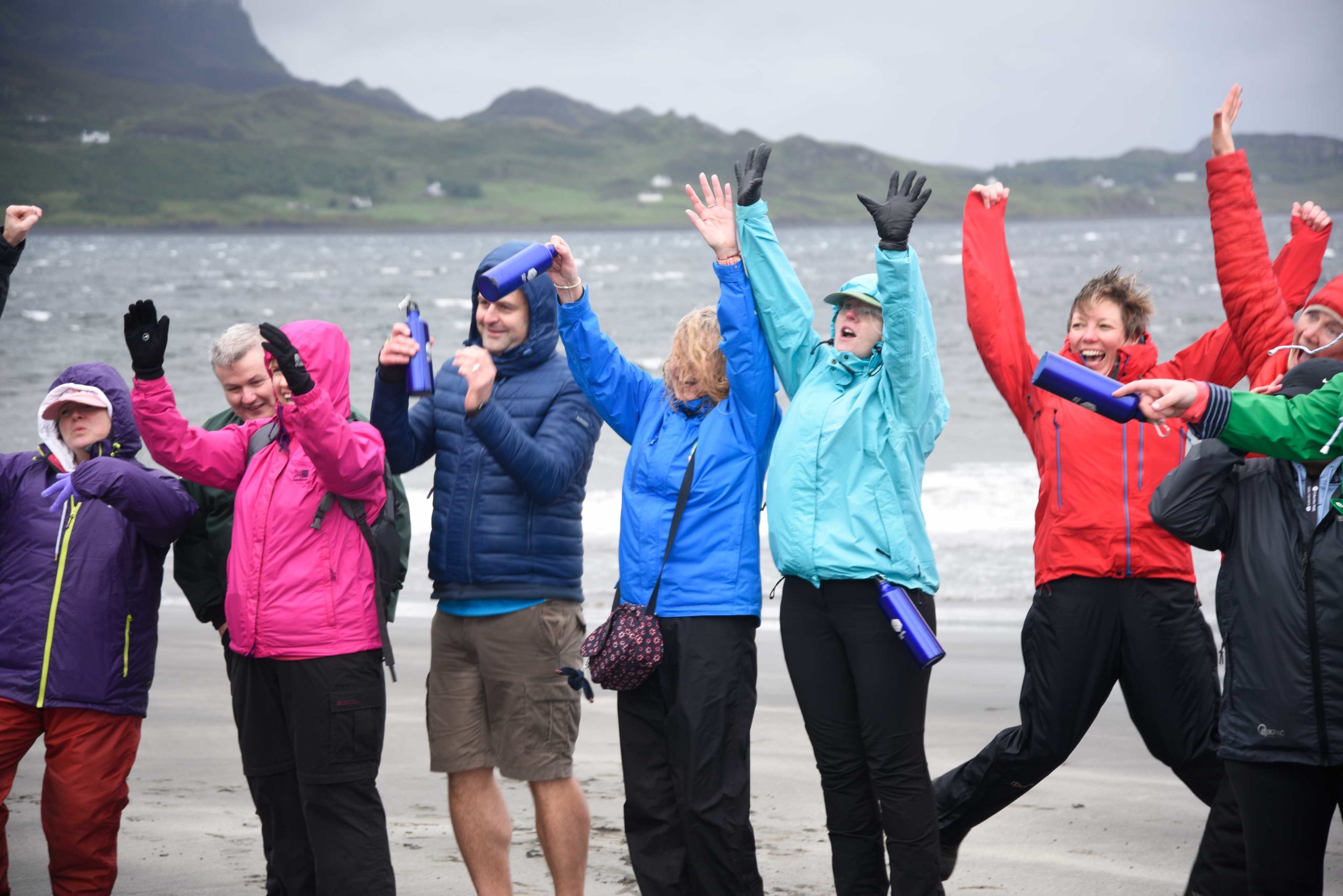 Group of adults jumping and cheering on a beach in Skye in the rain