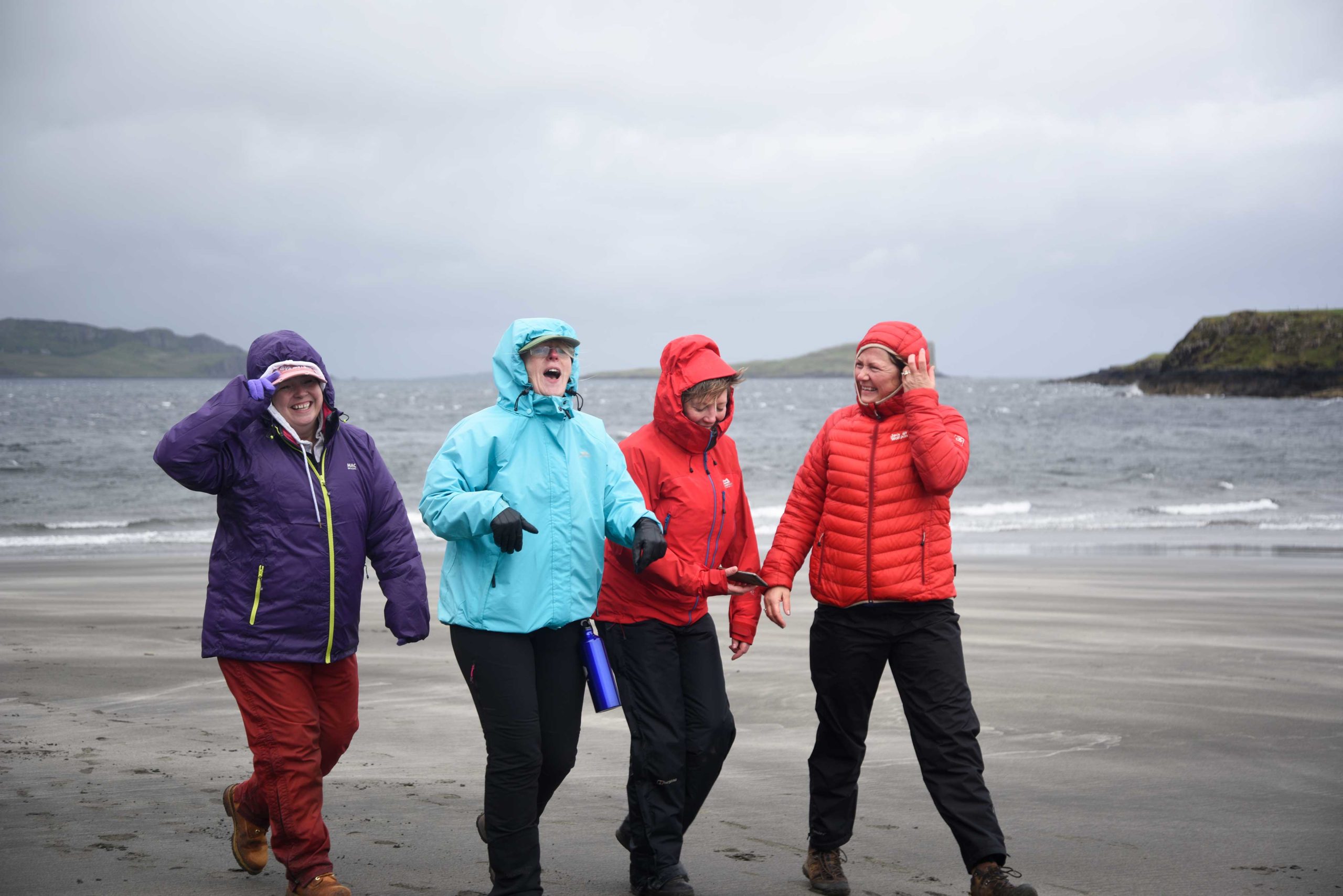 Four women walking in the rain along a beach on Skye