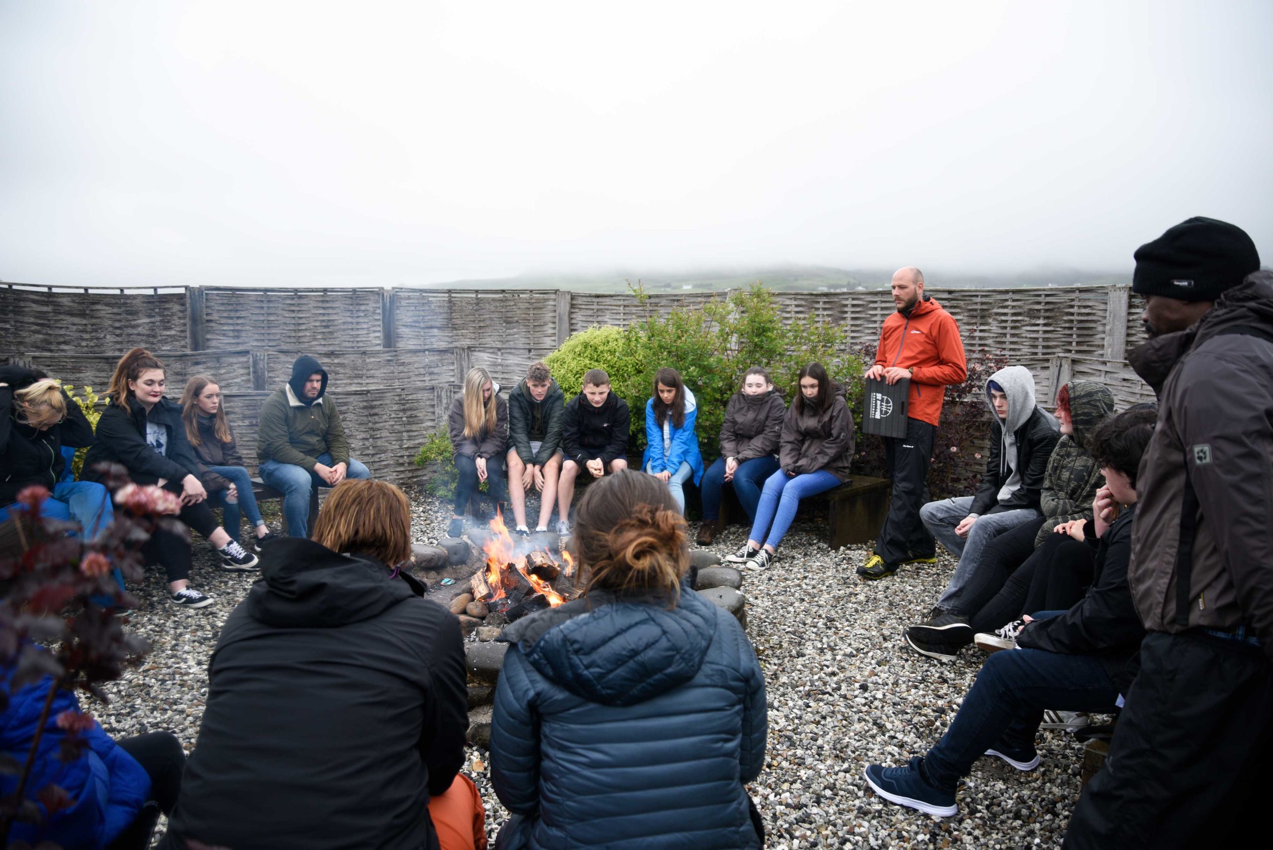 Large group of teenagers with instructor gathered round a campfire